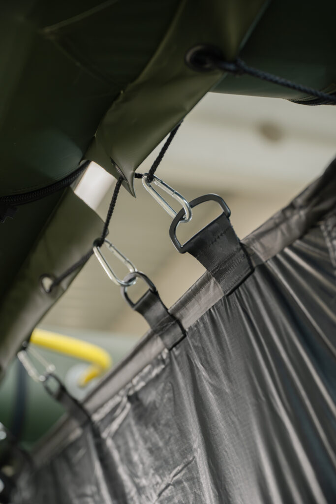 Detailaufnahme der Aufhängung einer Zeltwand mit Karabinerhaken an einem Zeltsystem.